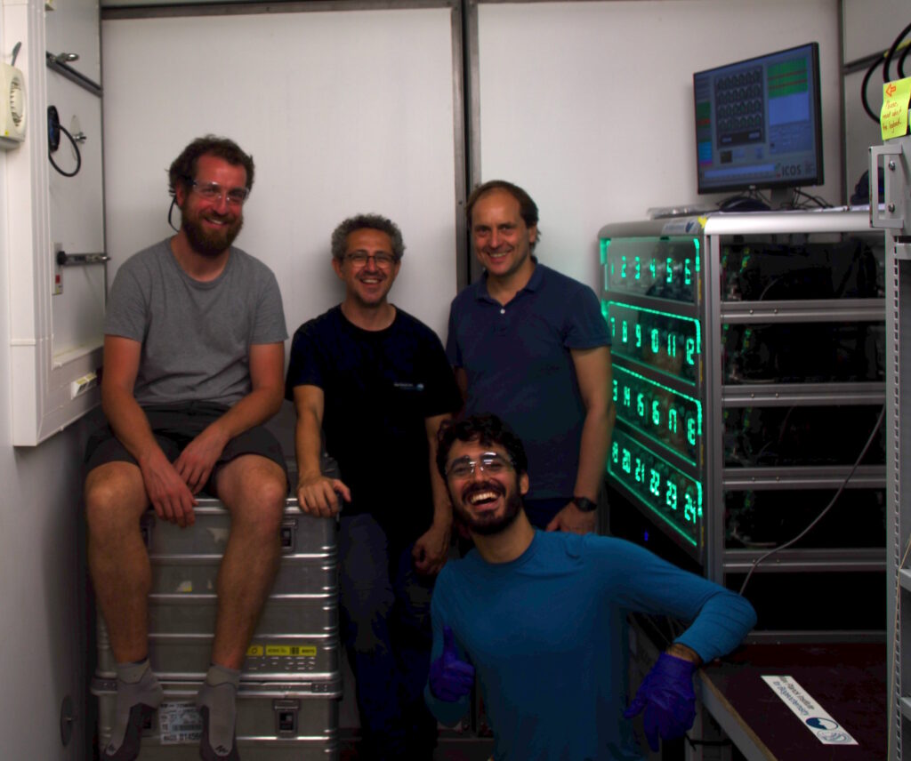 The team gathered in container next to the installed flask sampler, smiling into the camera.